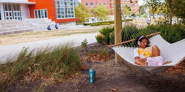 An african american studies degree student relaxes and studies in a hammock on KU's campus