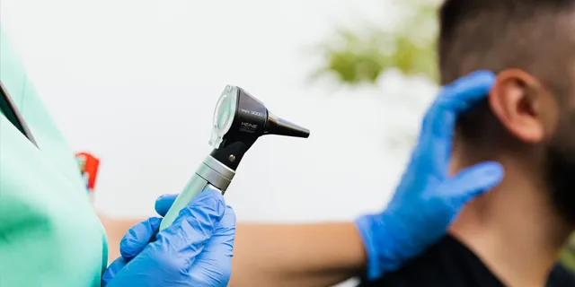 Student clinician in an audiology PhD degree program uses an otoscope to examine a patient's ear during healthcare training.