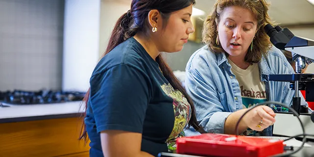 A chemistry degree student works with a KU faculty member conducting chemistry experiments in a lab