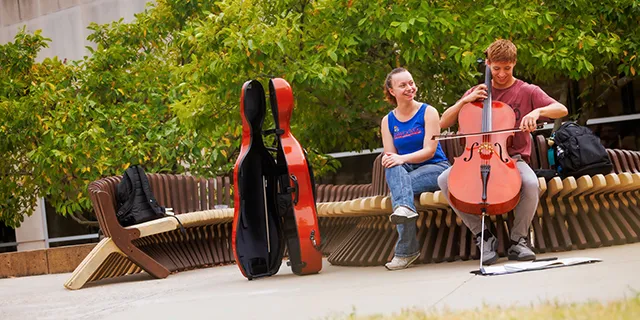 University of Kansas student playing the cello for a friend on campus
