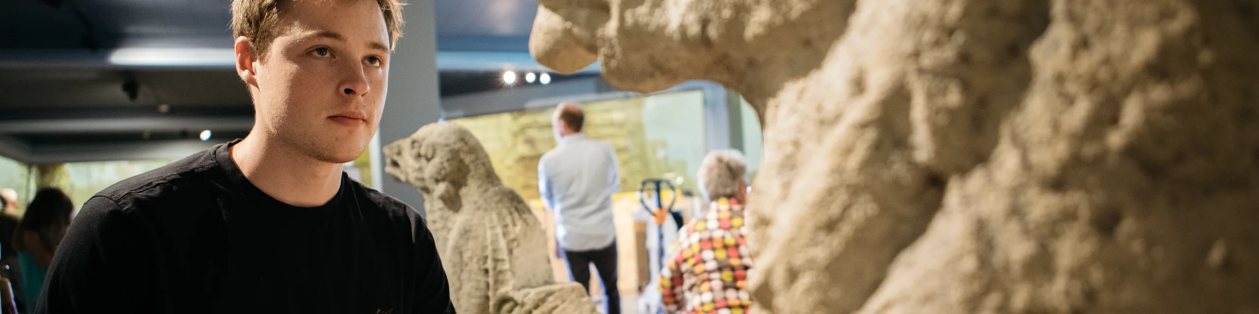 A KU graduate student sketches in a notebook while studying carved Eurasian stone figures displayed in a Slavic museum gallery.